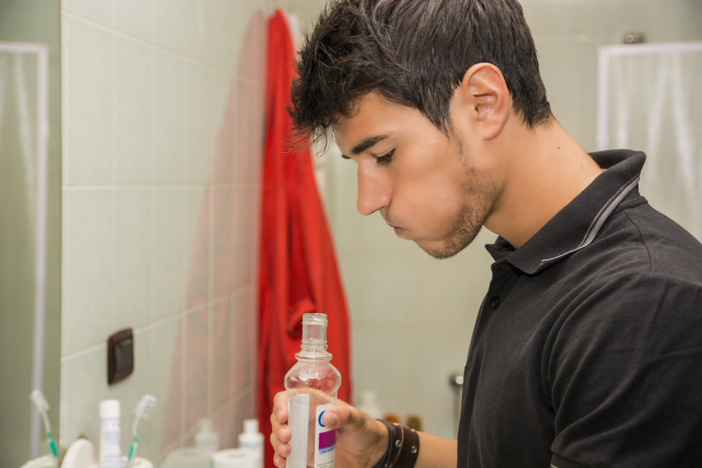 Close of of man wearing black shirt in bathroom rinsing with mouth wash