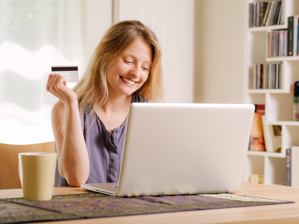 a young woman holding a credit card while using a laptop
